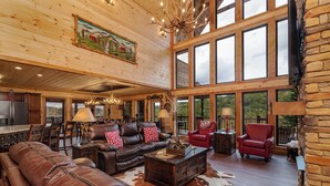 A spacious living room with a large leather sofa, red armchairs, and a wooden coffee table. There are large windows providing natural light and a view of the outdoors. - Near Dollywood + Resort Amenities Included (Pigeon Forge)