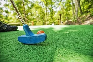 A close-up of a blue putter on a green artificial turf surface.