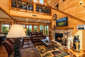 A spacious living area with leather sofas, a fireplace, and a large TV mounted on the wall.