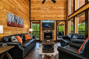 A log cabin interior with a fireplace, leather sofas, and a large painting on the wall.