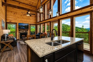 A spacious cabin interior with a kitchen island, dining area, and a fireplace.