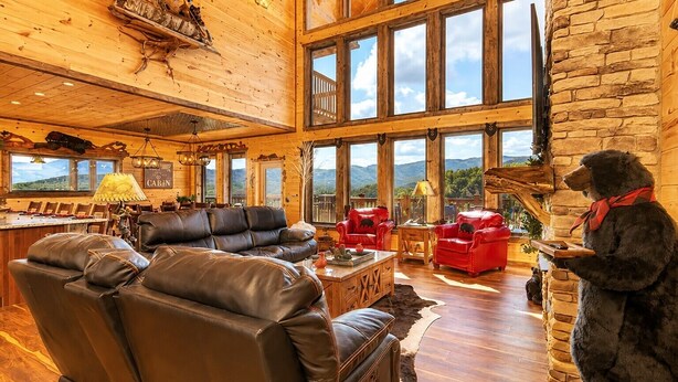 A spacious living room with leather sofas, a bear statue, and large windows offering mountain views. - Luxury Cabin w/ All-Inclusive Resort Amenities (Sevierville)