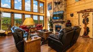 A spacious living room with large windows, a fireplace, and bear-themed decor. - Luxury Cabin w/ All-Inclusive Resort Amenities (Sevierville)