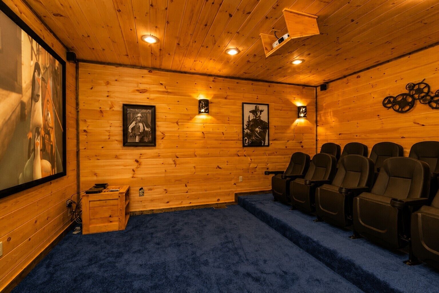 A wooden-paneled room with a blue carpet, a projector, and framed pictures on the walls.