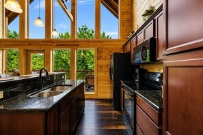 A modern kitchen with wooden cabinetry, a granite countertop, and a large window overlooking greenery.