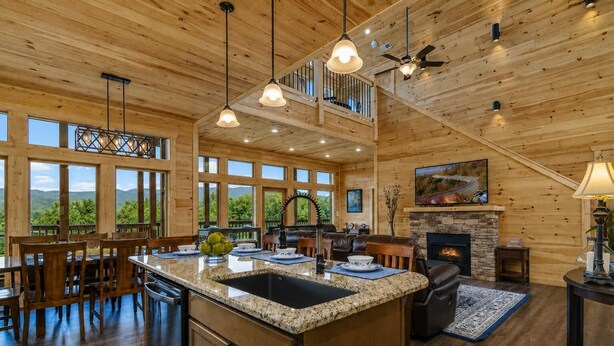 Une cuisine spacieuse dotée d’un grand îlot central, d’un plafond en bois et de grandes fenêtres offrant une vue sur l’extérieur.