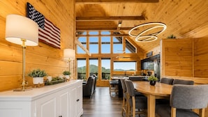 A wooden interior with a dining area, kitchen, and large windows offering a mountain view. - Luxury Cabin w/ All-Inclusive Resort Amenities (Sevierville)