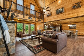 A spacious cabin interior with a stone fireplace, leather furniture, a dining area, and a kitchen. - Near Dollywood + Resort Amenities Included (Sevierville)