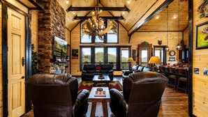 A spacious living room with leather chairs, a fireplace, and large windows offering a view of the outdoors. - Near Dollywood + Resort Amenities Included (Sevierville)