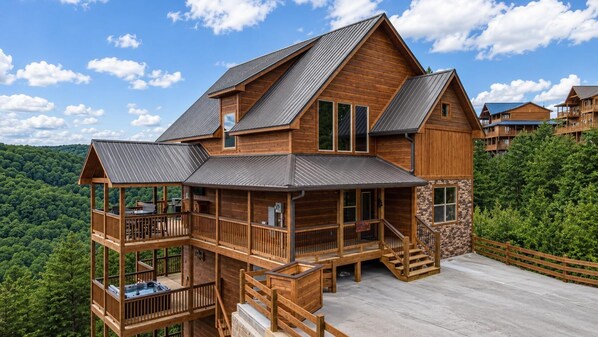 A multi-story wooden cabin with a balcony, a hot tub, and a stone wall.