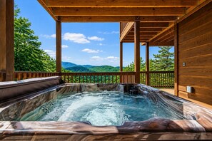 A hot tub with a wooden deck and a view of green hills.