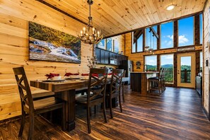 A wooden cabin interior with a dining area, kitchen, and a balcony with a view.