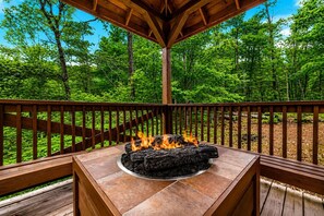 A wooden deck with a stone fire pit and a wooden railing.