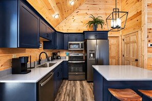 A modern kitchen with dark blue cabinets, stainless steel appliances, and a wooden ceiling.