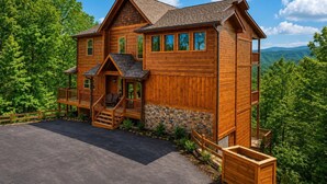 A wooden cabin with a stone foundation, a porch, and a view of the surrounding forest.