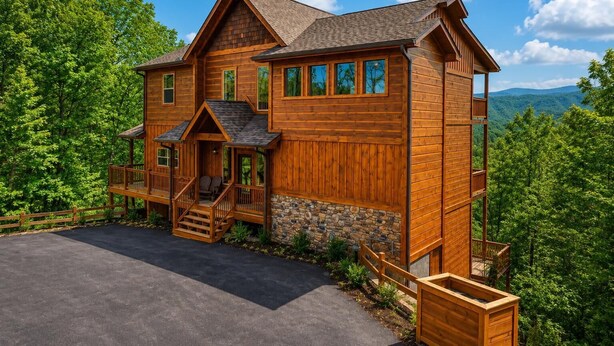 A wooden cabin with a stone foundation, a porch, and a view of the surrounding forest. - Luxury Cabin w/ All-Inclusive Resort Amenities (Pigeon Forge)