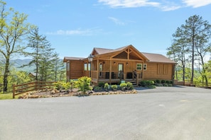 A wooden cabin with a porch, surrounded by trees and a mountain view. - Cabin + FREE Resort Amenities | Pigeon Forge (Pigeon Forge)