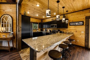 A kitchen with a large granite island, dark cabinetry, and a 'Thankful' sign.