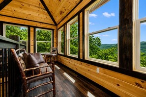 A wooden interior with large windows, a wooden ceiling, and a view of green trees.