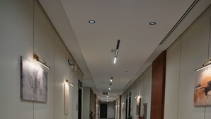 Ein langer, schmaler Korridor mit Teppichboden, eingelassener Beleuchtung und gerahmten Kunstwerken an den Wänden.