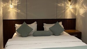 A modern bedroom with a large bed, two wall-mounted lights, and a wooden headboard. - Park Alasema (Riyadh)