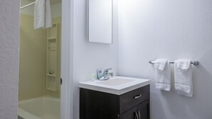 A bathroom with a white sink, dark cabinet, and a mirror. There are two towels hanging on the wall. - The Driftwood Lodge (Juneau)
