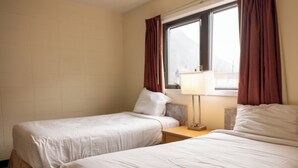 A hotel room with two beds, a nightstand with a lamp, and a window with curtains. - The Driftwood Lodge (Juneau)