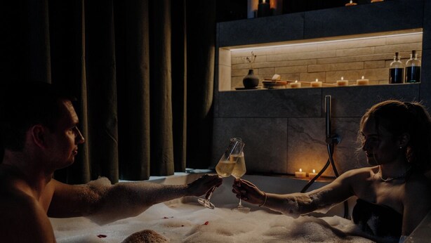 Un couple dans un jacuzzi, avec des bougies et des bouteilles en arrière-plan.