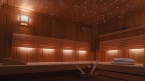 Un sauna avec des murs et des bancs en bois, un radiateur fixé au mur et un petit seau avec une brosse.