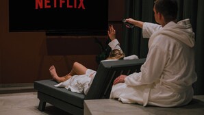 Une personne est assise sur un canapé et regarde la télévision. Le mot « NETFLIX » apparaît à l’écran.