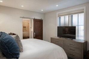 Un dormitorio con una cama, un televisor sobre una cómoda, una puerta corredera y una ventana.