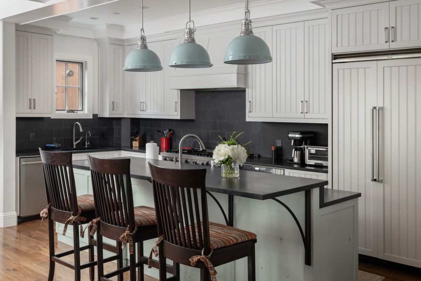 A modern kitchen with white cabinetry, a central island with bar stools, and pendant lighting.
