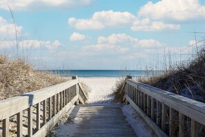 A wooden boardwalk leading to a sandy beach with a clear sky and clouds.