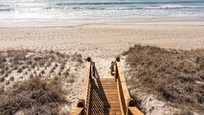 Une promenade en bois qui mène à une plage de sable et offre une vue sur l’océan.