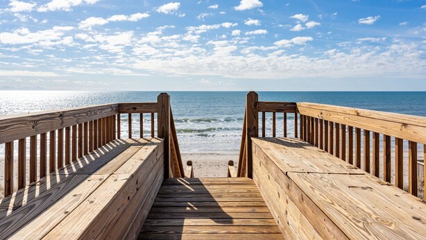 Une promenade en bois menant à une plage, avec un ciel dégagé.