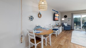 A dining area with a wooden table and white chairs, a hanging woven light fixture, and a view of the outdoors through a sliding glass door. - Blue Oar- Beach, Pool, and Sun in Surf City! (Surf City)