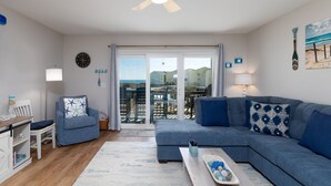 A living room with a blue sofa, a white armchair, a coffee table, and a ceiling fan. - Blue Oar- Beach, Pool, and Sun in Surf City! (Surf City)