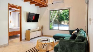 A modern living room with a TV, a large window, a green sofa, and a round coffee table.