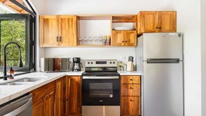 A kitchen with wooden cabinets, a stainless steel refrigerator, a built-in oven, and a window with a view of greenery.