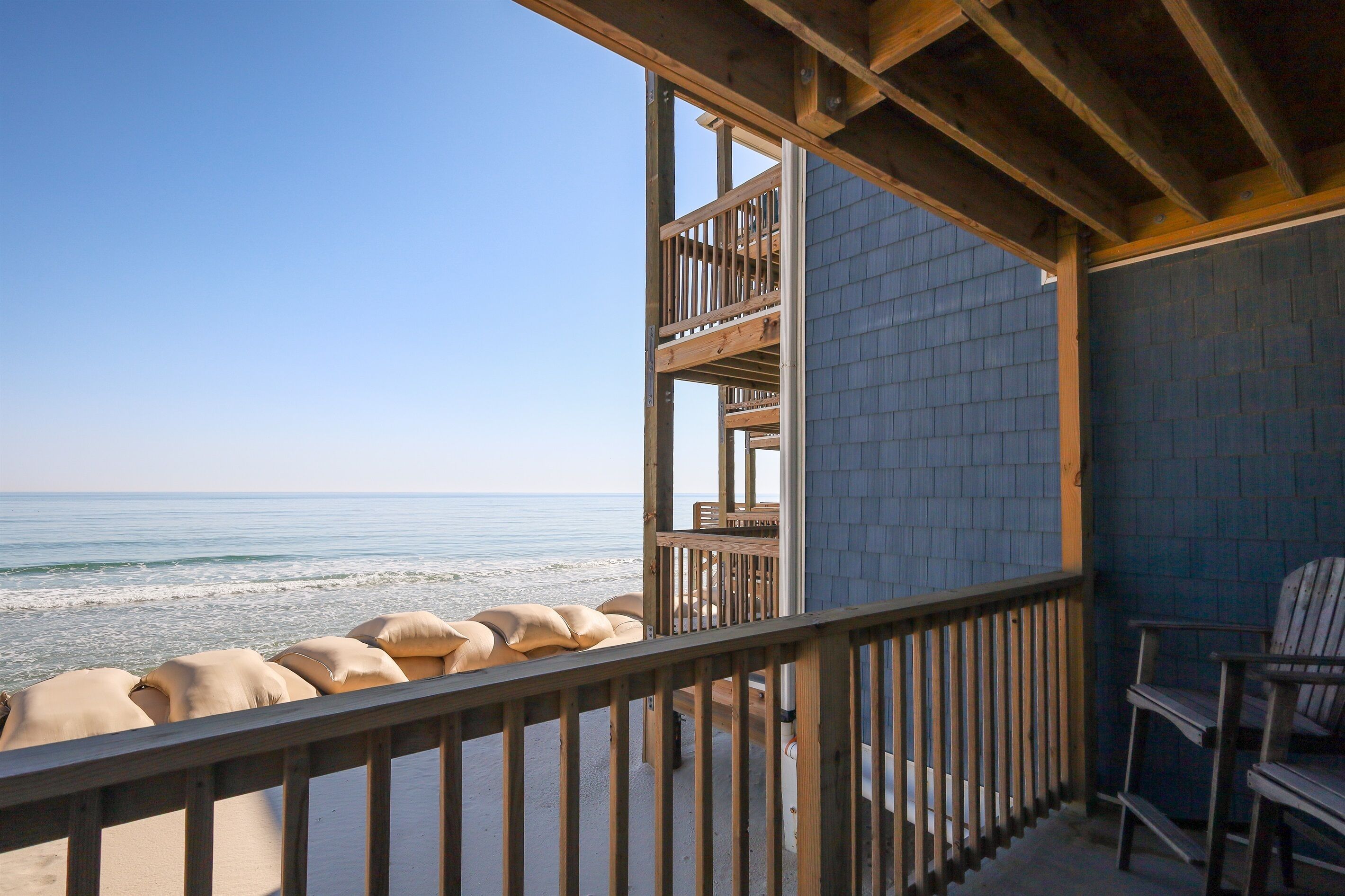 Ein Holzbalkon mit Blick aufs Meer, eine blaue Wand und ein Stuhl.