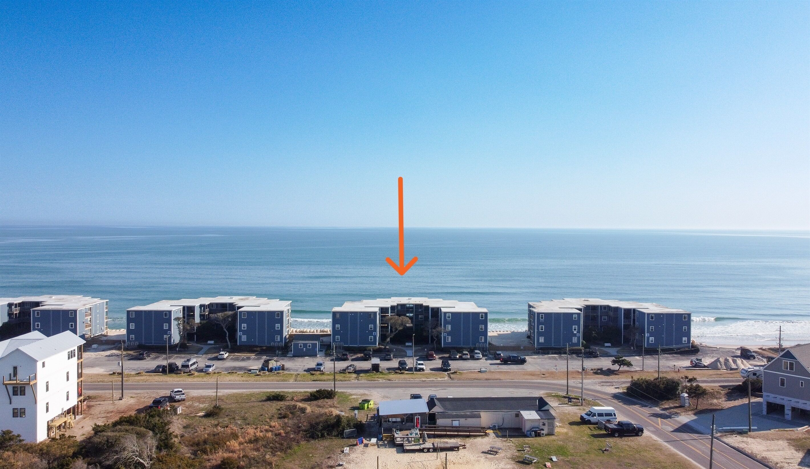 Een kustgebied met woonhuizen, meerdere blauwe gebouwen, een weg en helder uitzicht op de oceaan.