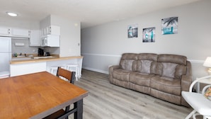 A compact living space with a kitchenette, a dining area, and a seating area with a sofa and a chair. - Sun of a Beach- Your Ultimate Beachy Getaway (North Topsail Beach)