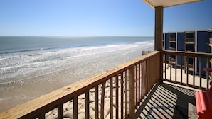 A wooden balcony overlooking a beach with waves, a clear sky, and a building with blue walls and wooden railings. - Sun of a Beach- Your Ultimate Beachy Getaway (North Topsail Beach)