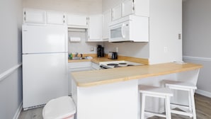 A compact kitchen with white cabinetry, a built-in microwave, a stove, and a wooden countertop. There are two white stools and a white sink. - Sun of a Beach- Your Ultimate Beachy Getaway (North Topsail Beach)