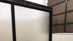 A bathroom with a frosted glass partition, white tiled walls, and a black metal frame.