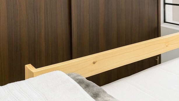 A bed with a wooden frame and a white mattress, a wooden headboard, and a dark wooden wardrobe.