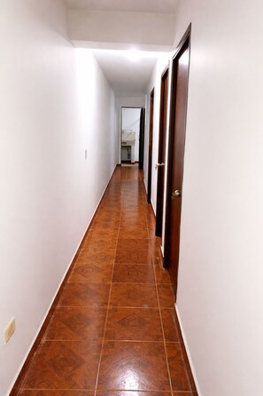 Un pasillo largo y estrecho con suelo de baldosas y puertas de madera a un lado.