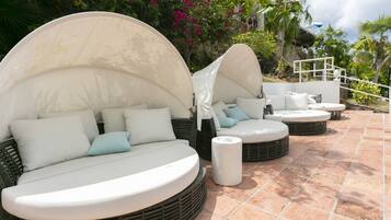 A patio with outdoor seating, including round and semi-circular couches with white cushions and a white umbrella.