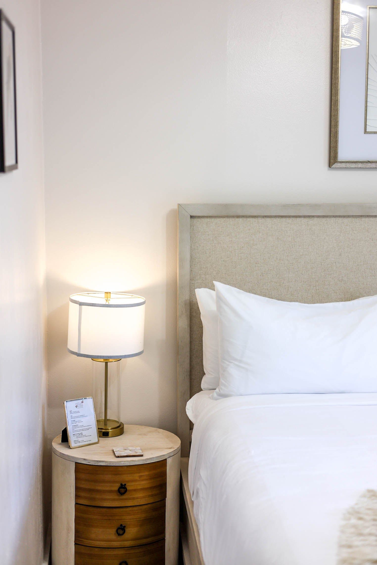 Habitación de hotel con una cama, una mesita de noche con lámpara y un espejo montado en la pared.