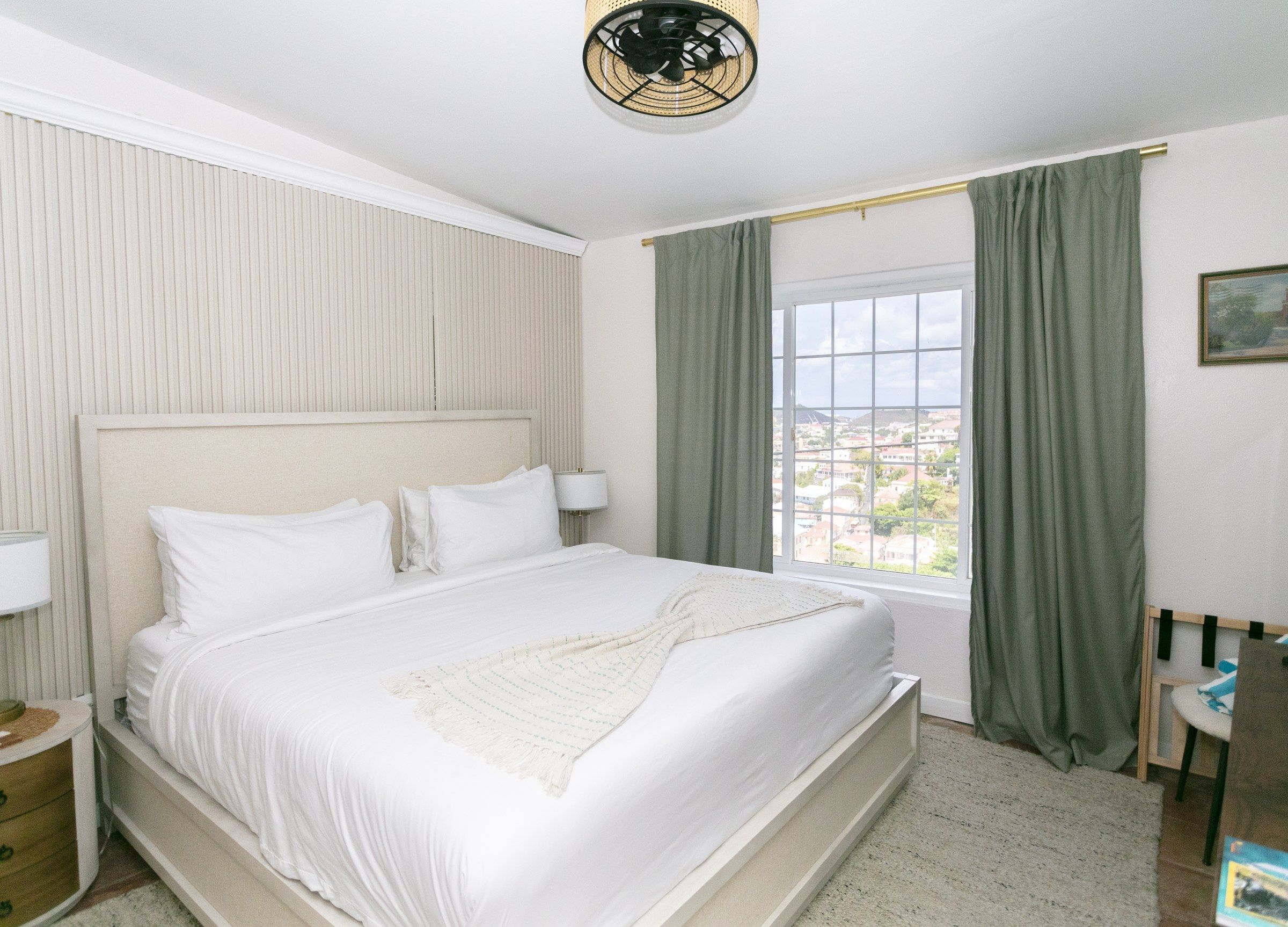 A hotel room with a large bed, a window with curtains, a bedside lamp, and a view of the cityscape.